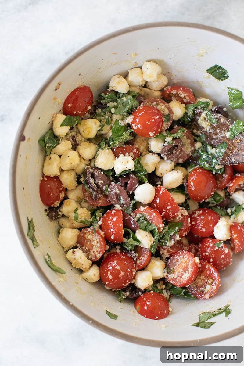 A vibrant close-up of Summer Pasta Salad with cherry tomatoes, Kalamata olives, and fresh basil leaves visible.