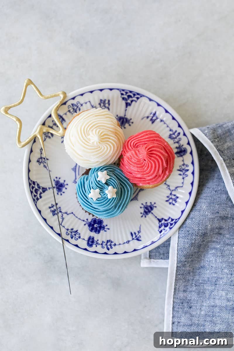 Three mini red, white, and blue cupcakes on a blue plate with a star sparkler, ready for celebration