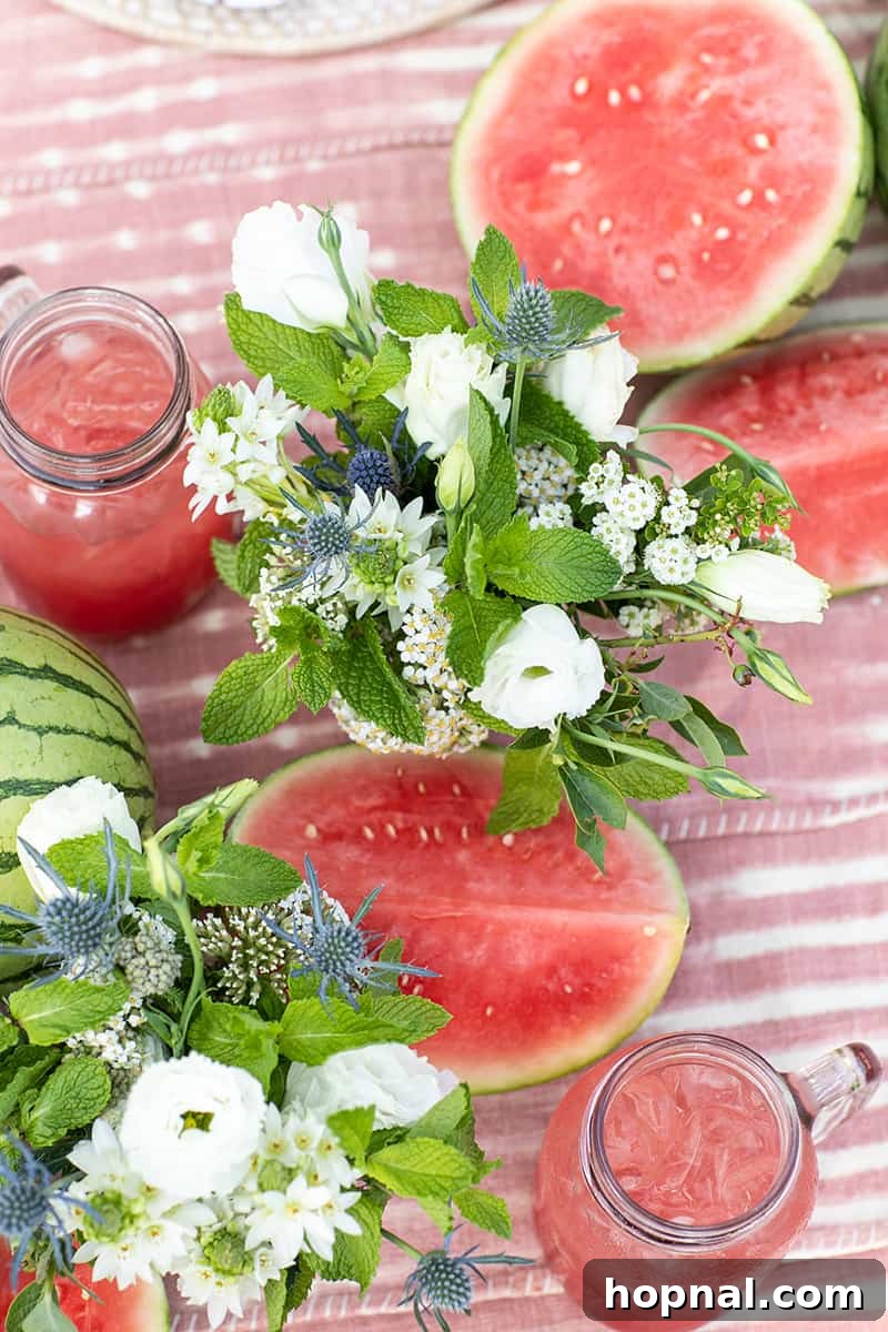 A beautifully arranged 4th of July table setting featuring a white and blue floral arrangement, fresh watermelons, and a pink-dyed tablecloth creating a vibrant and festive atmosphere.