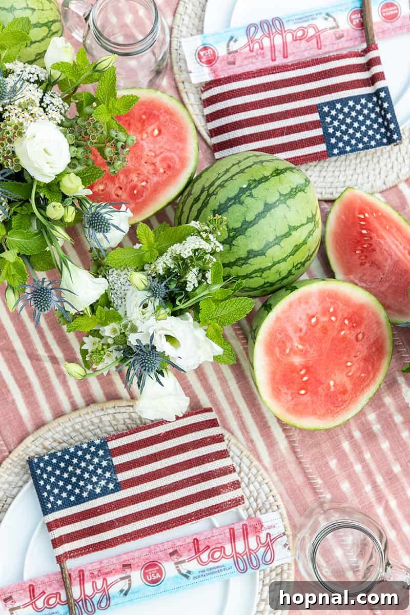 A beautifully set 4th of July party table adorned with charming flowers, fresh watermelon, a small burlap flag, and old-fashioned taffy, creating a rustic yet festive ambiance.