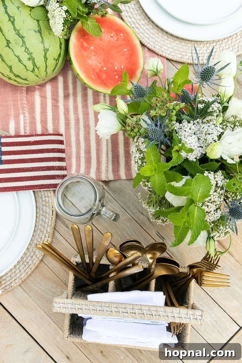 An inviting outdoor 4th of July party setup featuring elegant floral arrangements, a neatly organized silverware caddy, and festive decorations, ready for guests.