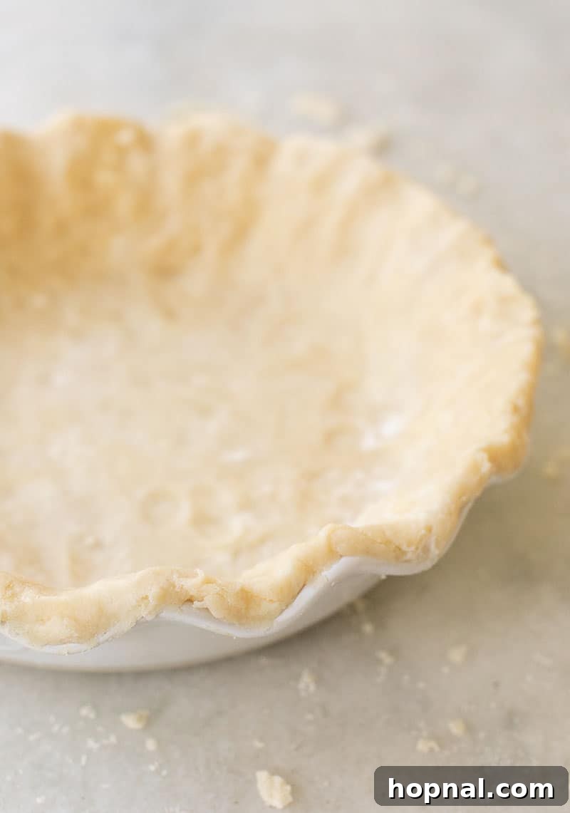 A perfectly formed, unbaked easy buttery pie crust resting in a pristine white ceramic pie dish, poised for filling and baking.