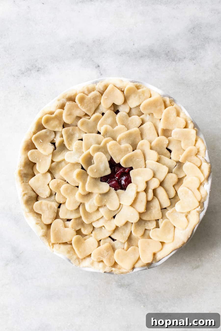 Overhead view of a beautifully shaped pie crust decorated with small heart cutouts, ready for baking, resting on a rustic wooden surface.
