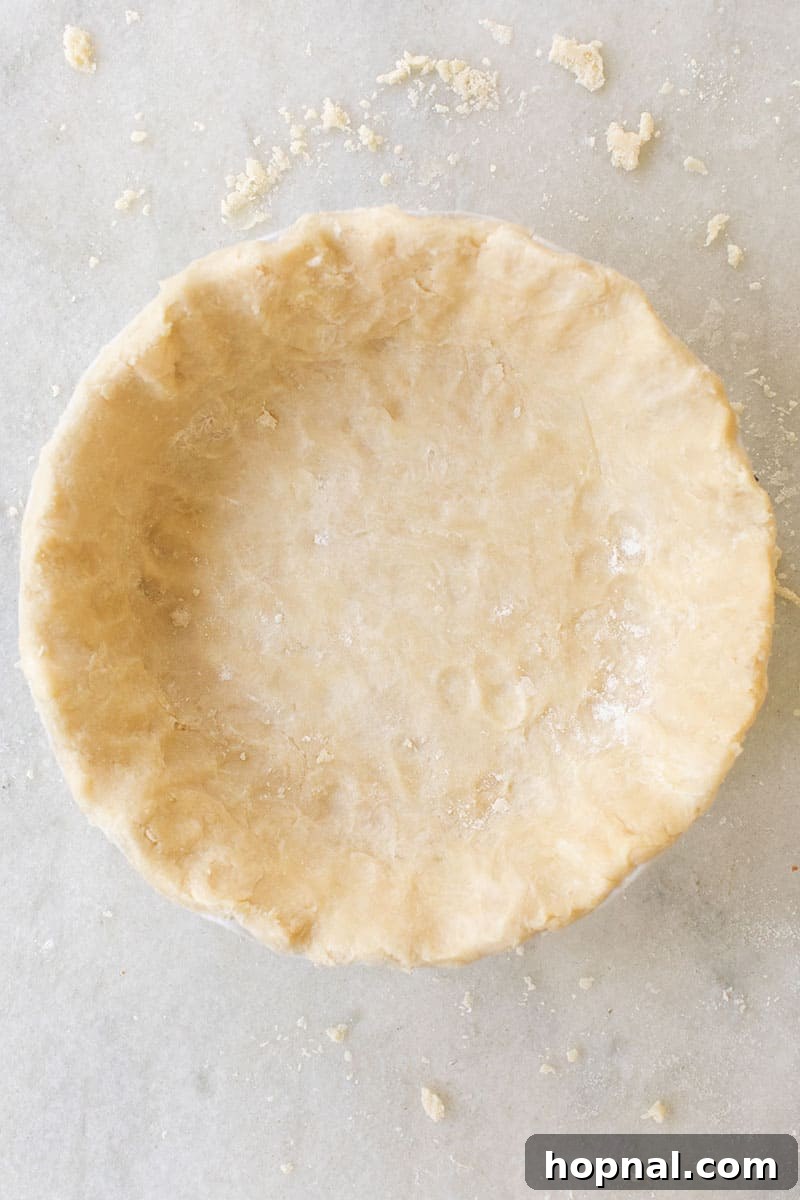 Overhead shot of a beautifully formed, unbaked pie crust resting in a pie dish on a marble countertop, showcasing its smooth, ready-to-bake texture.