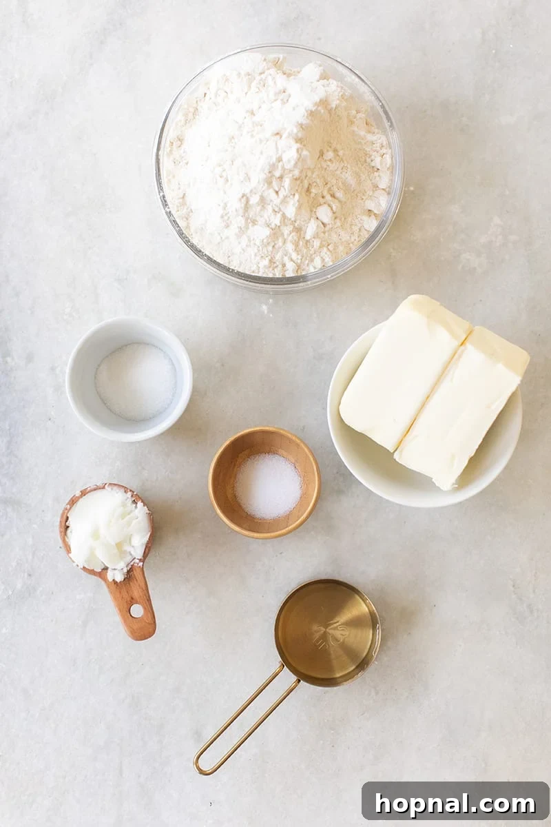 Essential ingredients for pie crust: cubes of cold butter, all-purpose flour, salt, sugar, and a glass of ice water, neatly arranged on a marble surface.