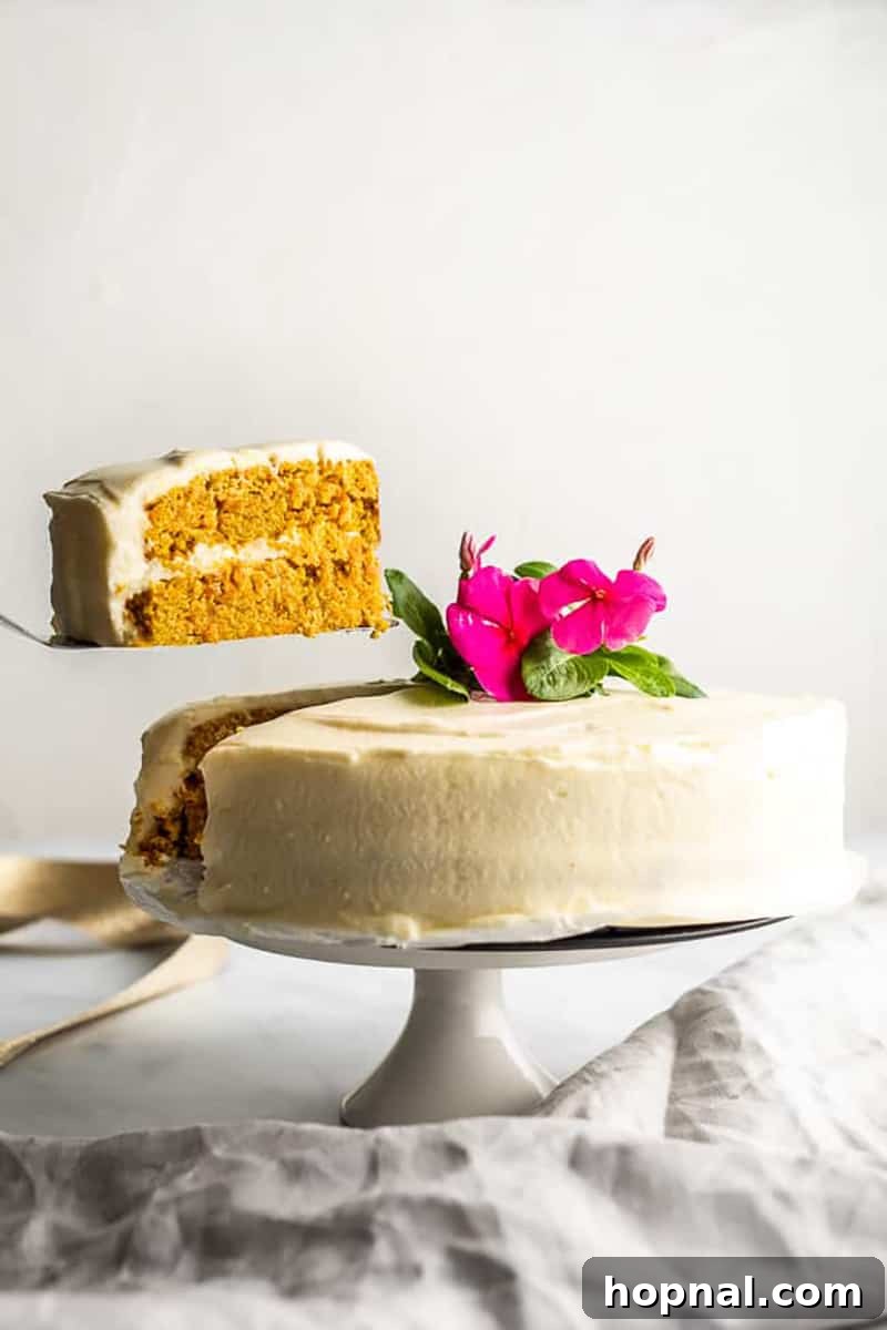 A beautiful slice of Keto carrot cake being removed from a whole cake, showing its moist texture and rich frosting.