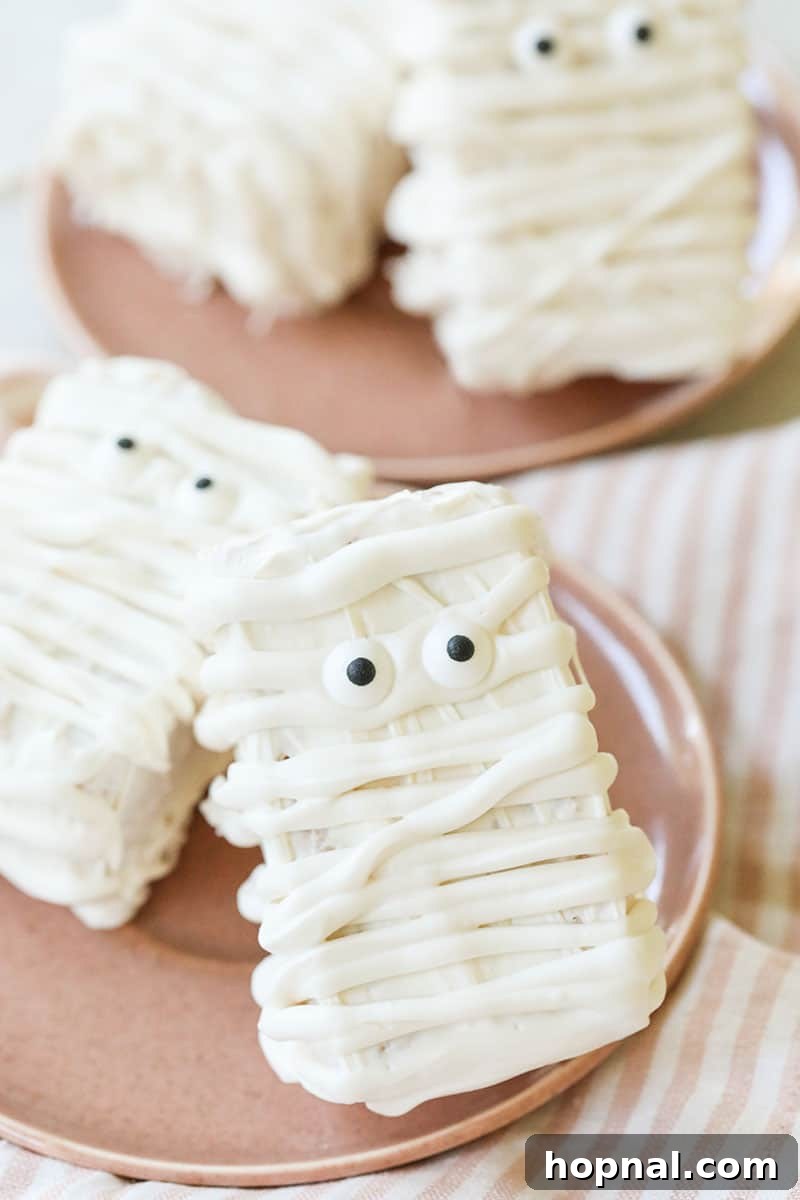 Brown Butter Mummy Rice Krispie Treats with white chocolate and candy eyes arranged on a wooden board.