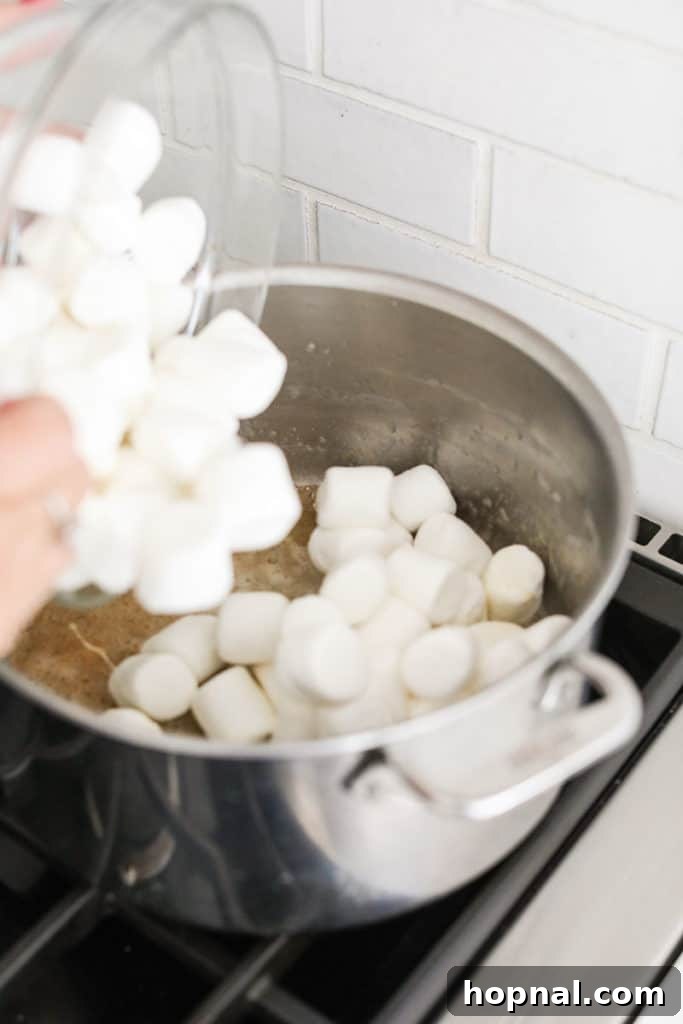 Pouring fresh marshmallows into the saucepan with browned butter, ready to melt.