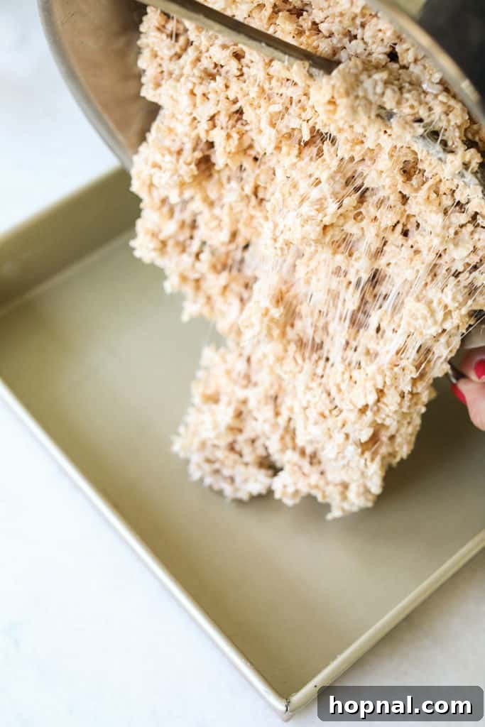 Pouring the sticky Rice Krispie treat mixture into a prepared 9x13 inch pan.