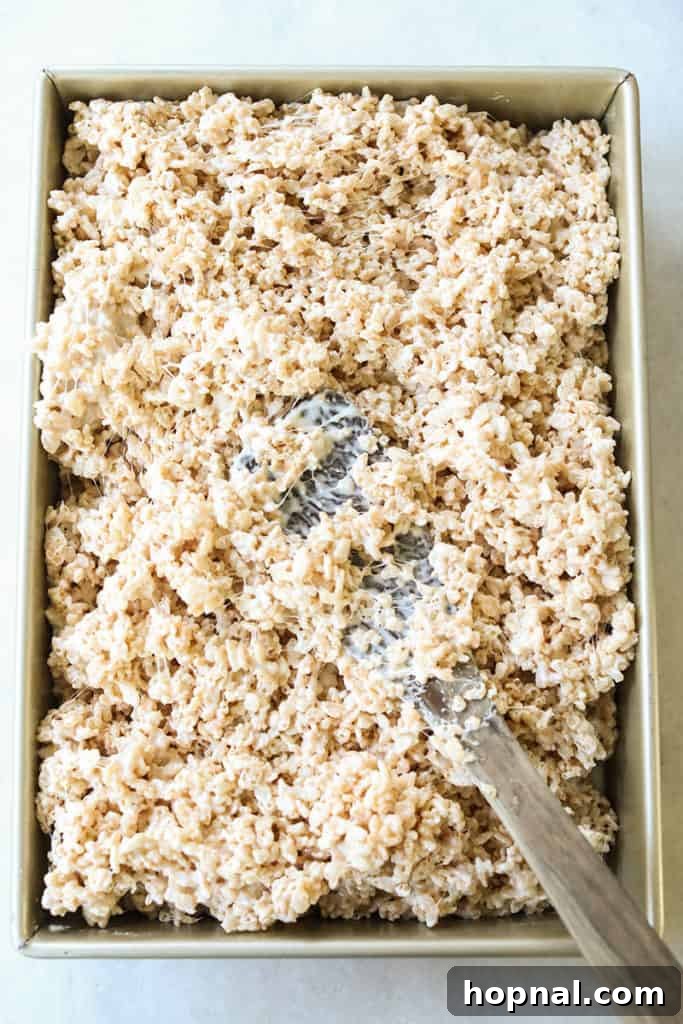 Gently pressing the Rice Krispie mixture evenly into the pan with a spatula.