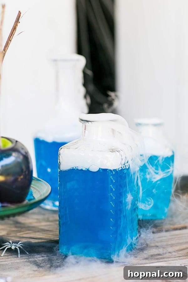 A vibrant blue cocktail with a smoky dry ice effect, served in a spooky bottle for a Halloween party.