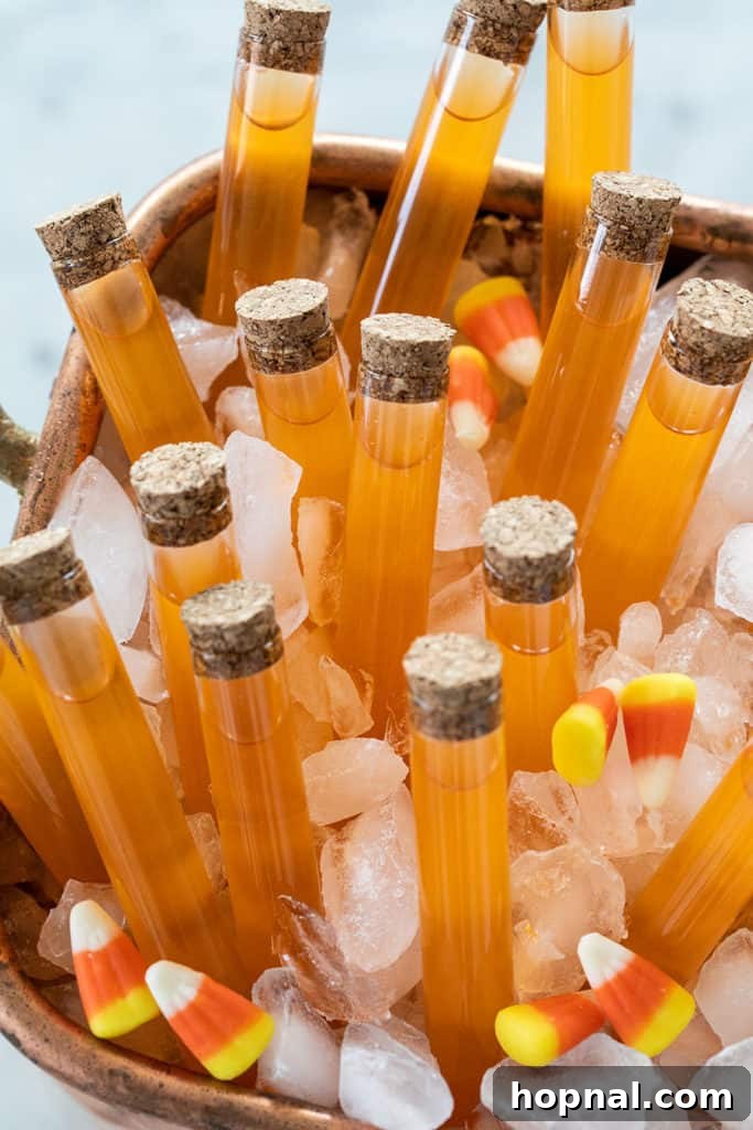 Clear shot glasses filled with vibrant candy corn infused vodka, garnished with whole candy corn pieces for a Halloween party.