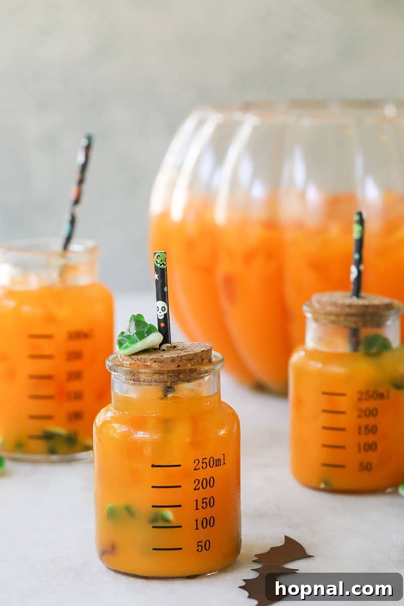 Kids Halloween punch recipe in little glass jars with straws, garnished with gummy worms and frogs.