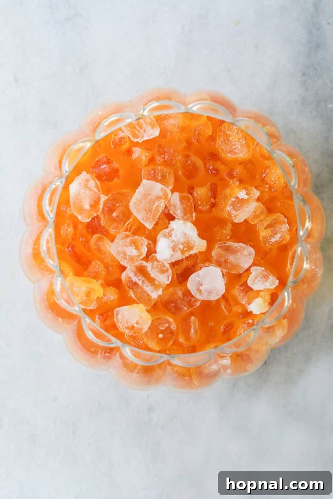 Adding ice to a Halloween punch for kids in a large punch bowl.