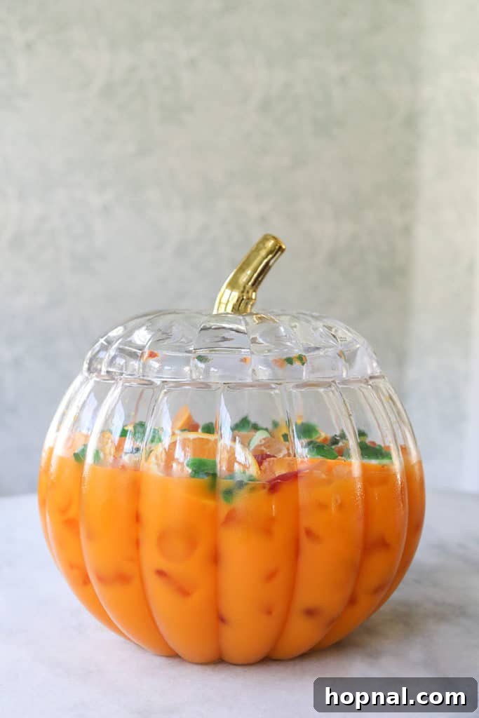Kids Halloween punch served in a pumpkin punch bowl with gummy worms and dry ice smoke.