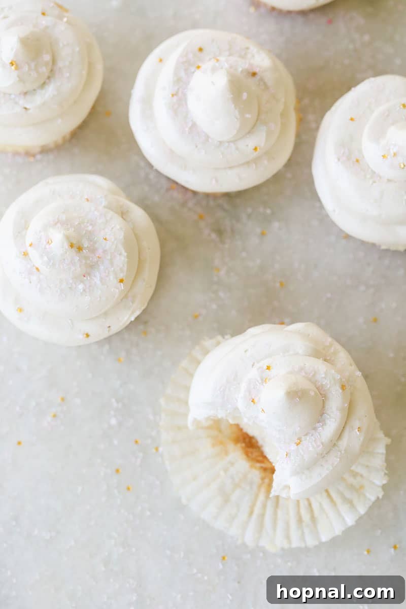 Five vanilla cupcakes overhead on a marble table with sprinkles.