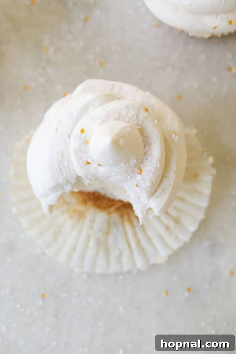 Overhead shot of a delicious vanilla cupcake with a bite taken out, showcasing fluffy homemade buttercream on a elegant marble surface.