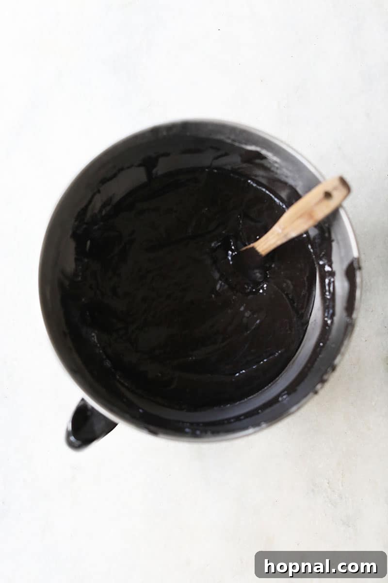 Dark black velvet cake batter in a mixing bowl on a marble table, showcasing the rich color achieved with black food coloring.
