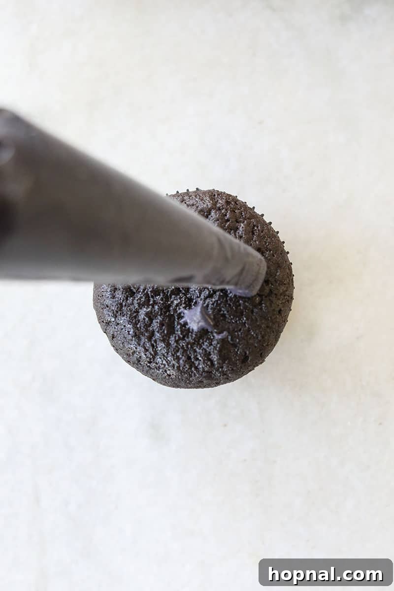 Piping fluffy black cream cheese buttercream frosting onto a black velvet cupcake, creating a smooth swirl.