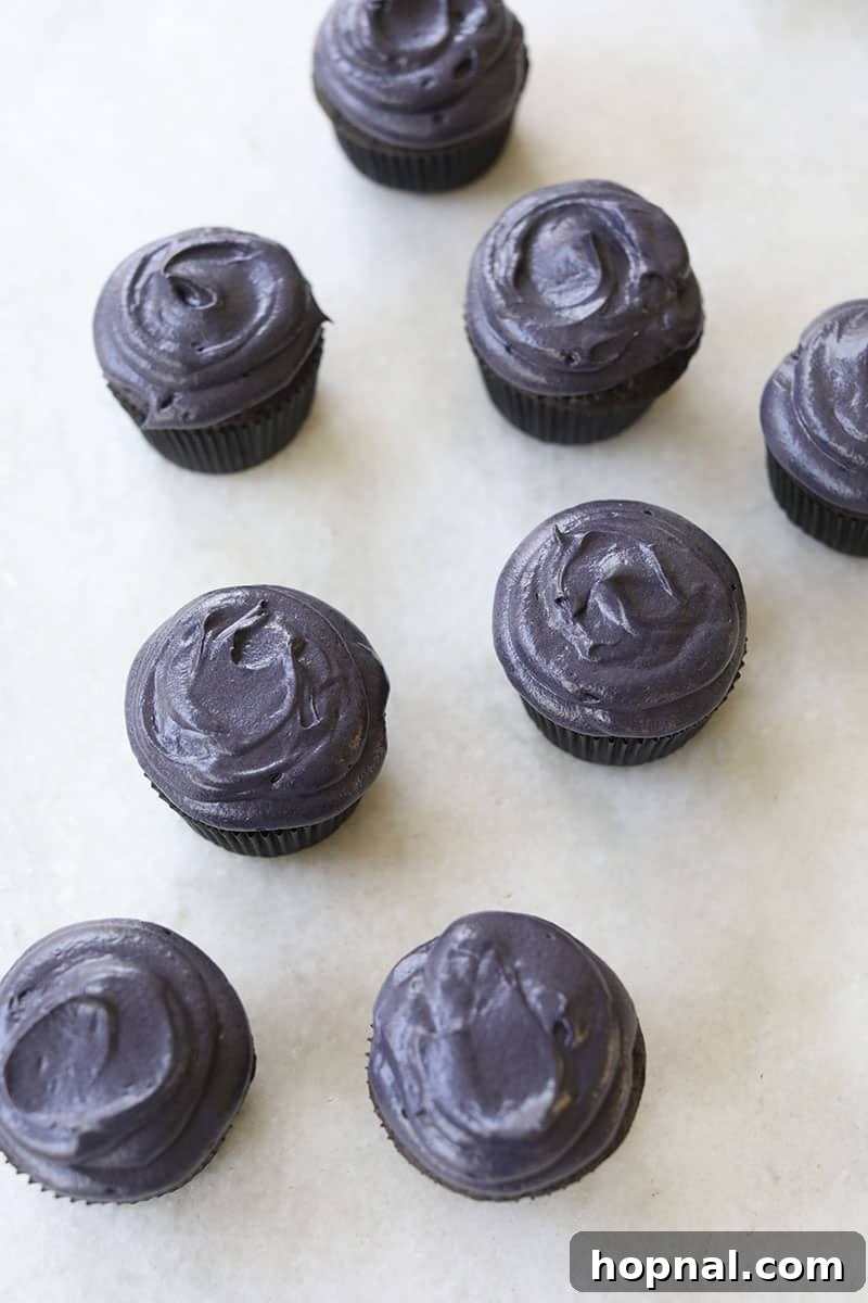 A tray of black velvet cupcakes topped with luxurious cream cheese frosting, showcasing their readiness for decoration.