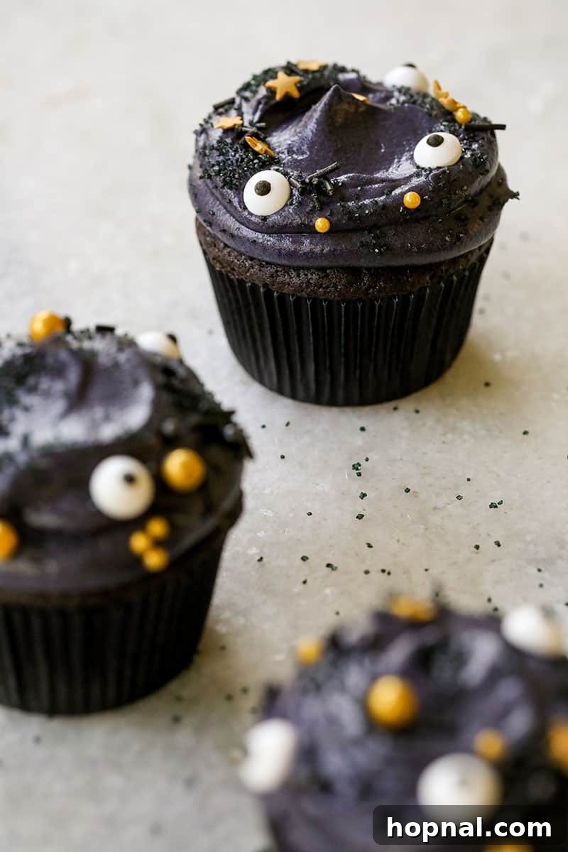 A tray of black velvet cupcakes topped with fluffy whipped cream cheese frosting and festive sprinkles, ready for a Halloween gathering.