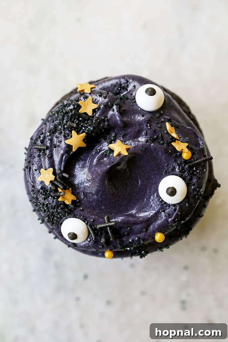 Black velvet cupcake topped generously with whipped cream cheese frosting and whimsical eyeball sprinkles, highlighting the dark cocoa powder base.