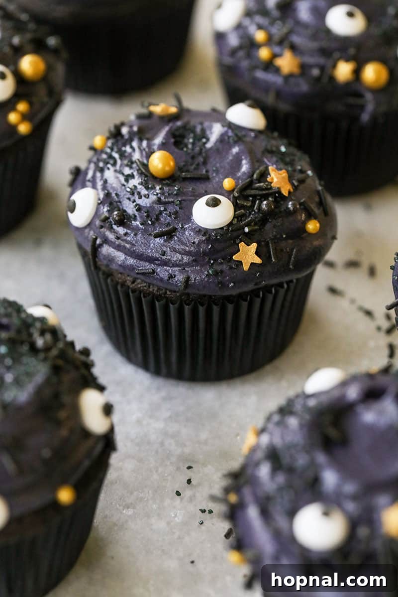 Spooky black velvet cupcakes in black cupcake liners, adorned with playful eyeball sprinkles and shimmering gold stars, perfect for a Halloween party.
