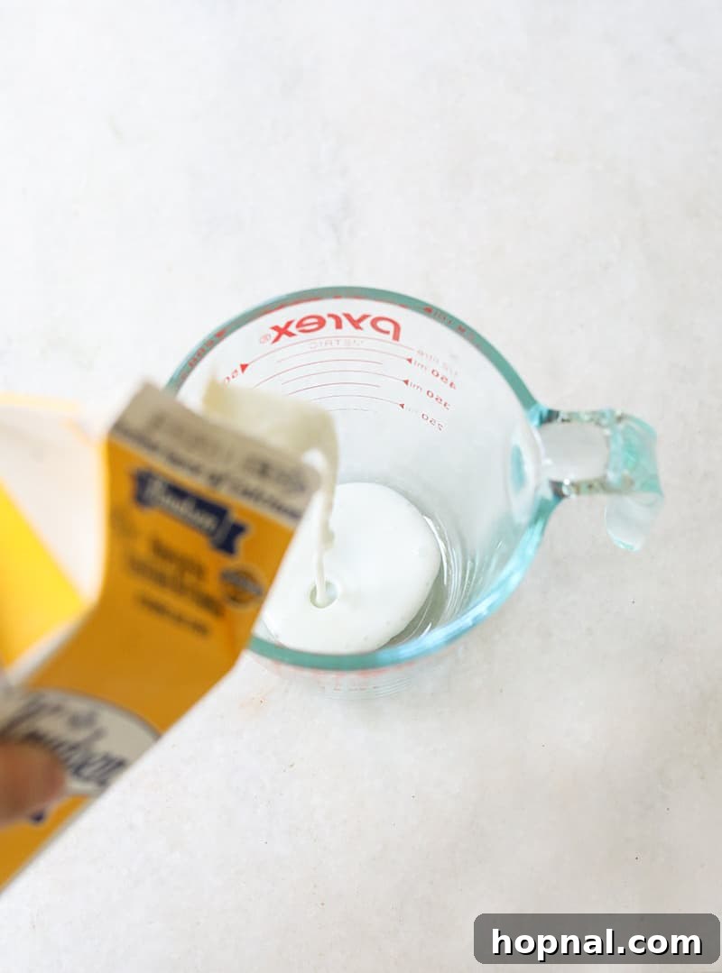 Buttermilk being poured into a clear glass measuring cup, highlighting a key liquid ingredient for black velvet cupcakes.