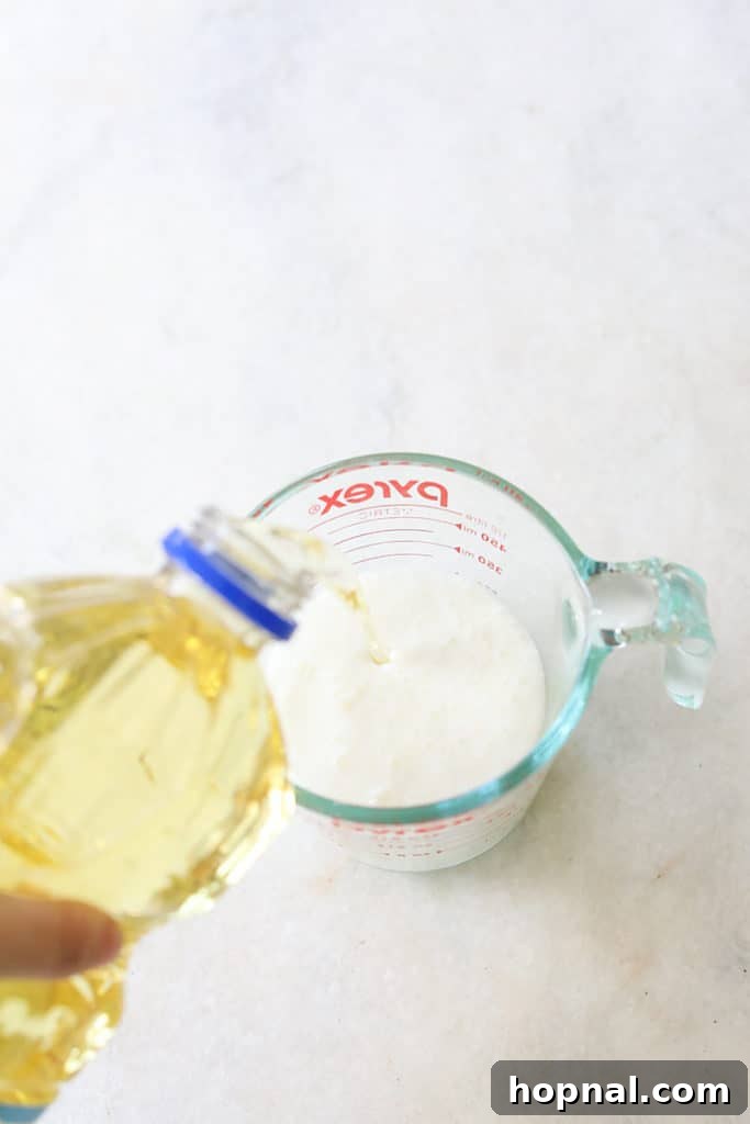 Pouring vegetable oil into a measuring cup, part of the wet ingredients for black velvet cupcakes.
