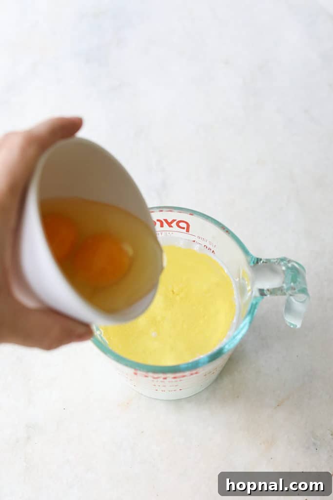 Two large eggs in a measuring cup, adding richness and structure to the cupcake batter.