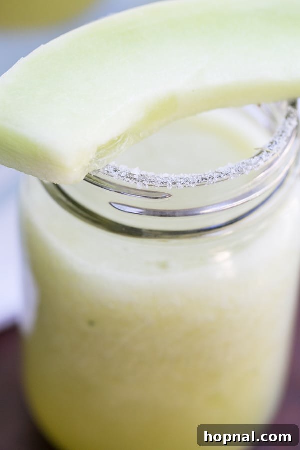 Honeydew slice on a fennel-salt rimmed glass with a refreshing frozen cocktail
