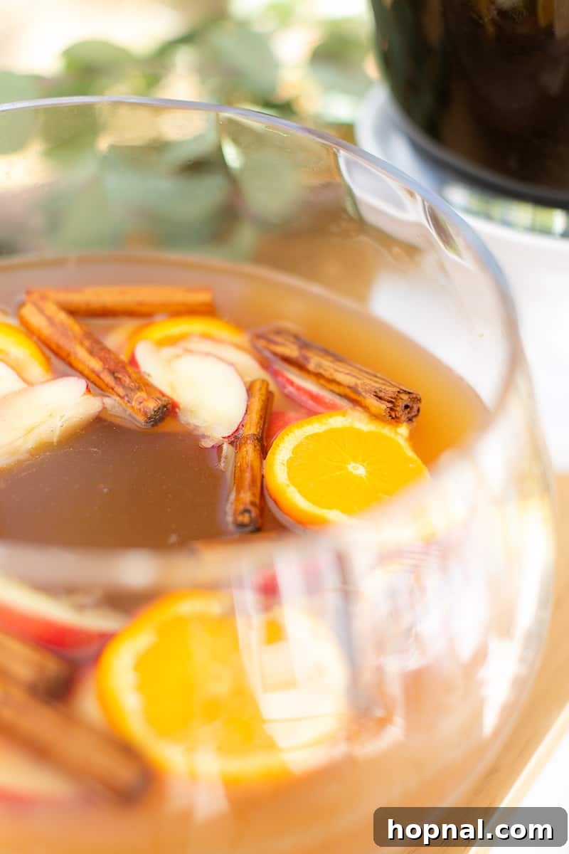 A festive cocktail punch, garnished with sliced apples and cinnamon sticks, served in an elegant punch bowl, perfect for a tea party.