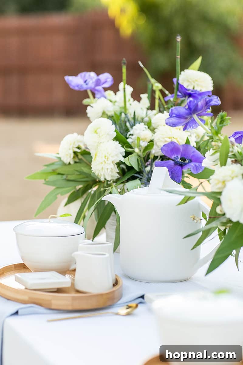 An elegant tea set, complete with a gleaming tea kettle and fresh floral accents, poised on a beautifully set table.