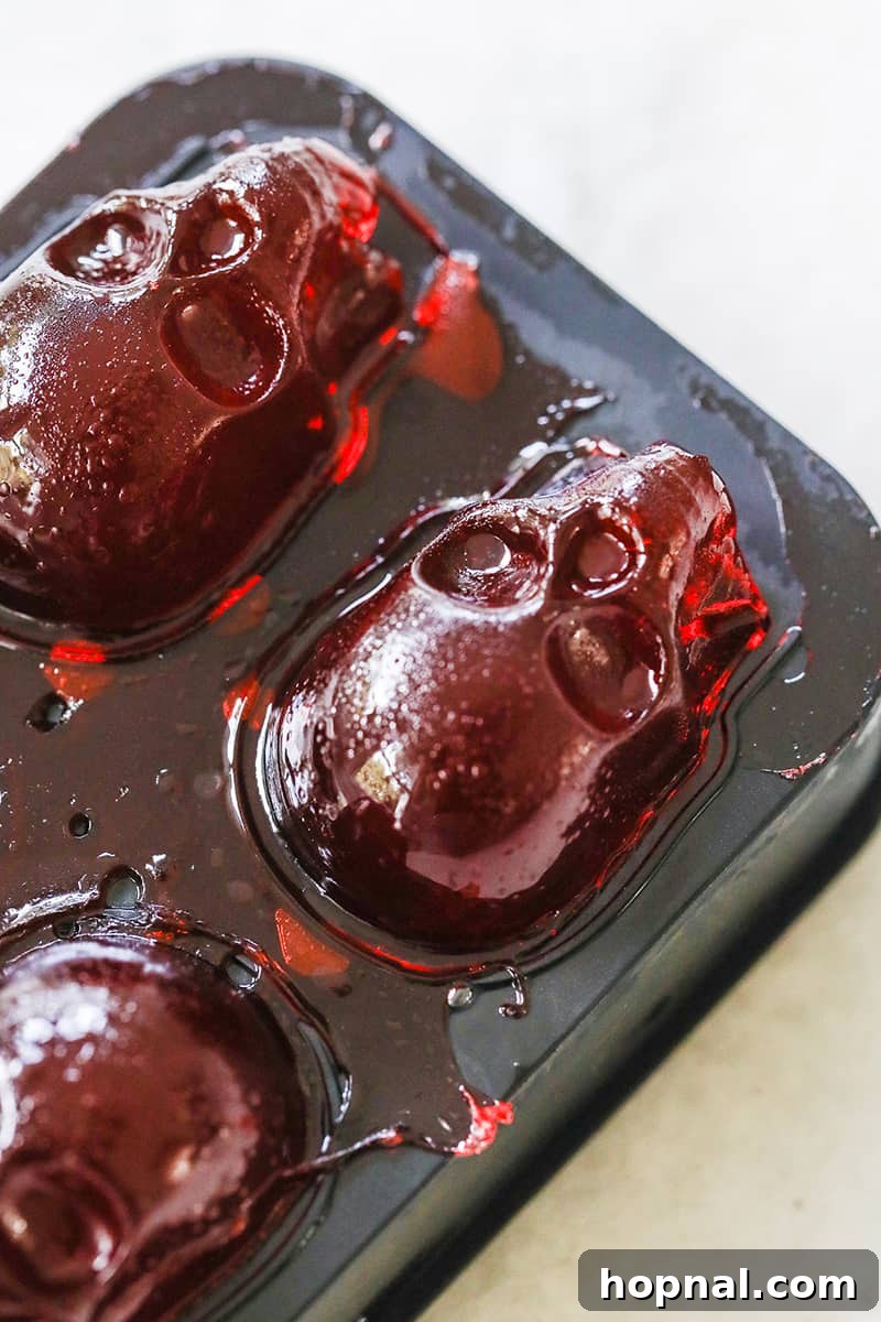Several skull jello shots are meticulously poured and beginning to set within a black silicone jello mold.