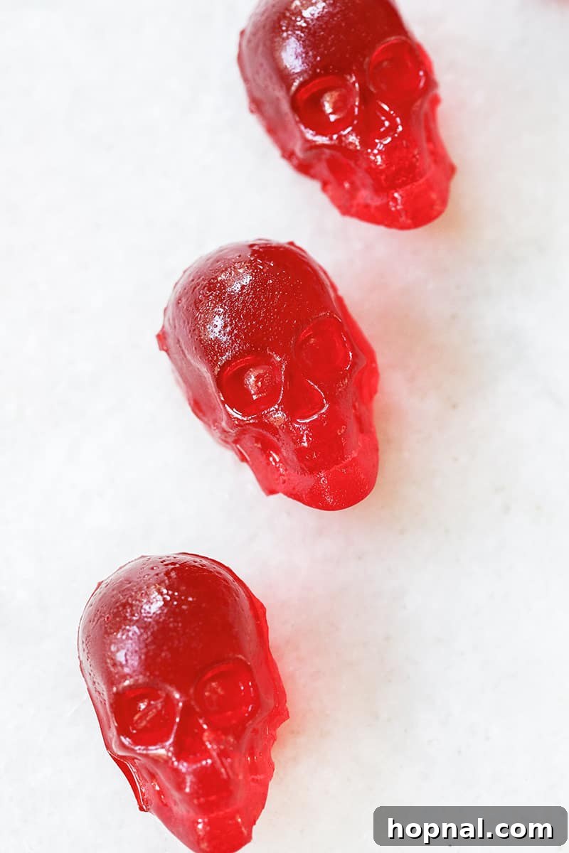 Vibrant red cherry jello shots, expertly shaped like skulls, are artfully displayed on an elegant marble table surface.
