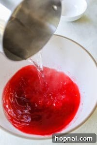 Boiling water being poured into a bowl with jello, vodka, and gelatin, all being whisked together.