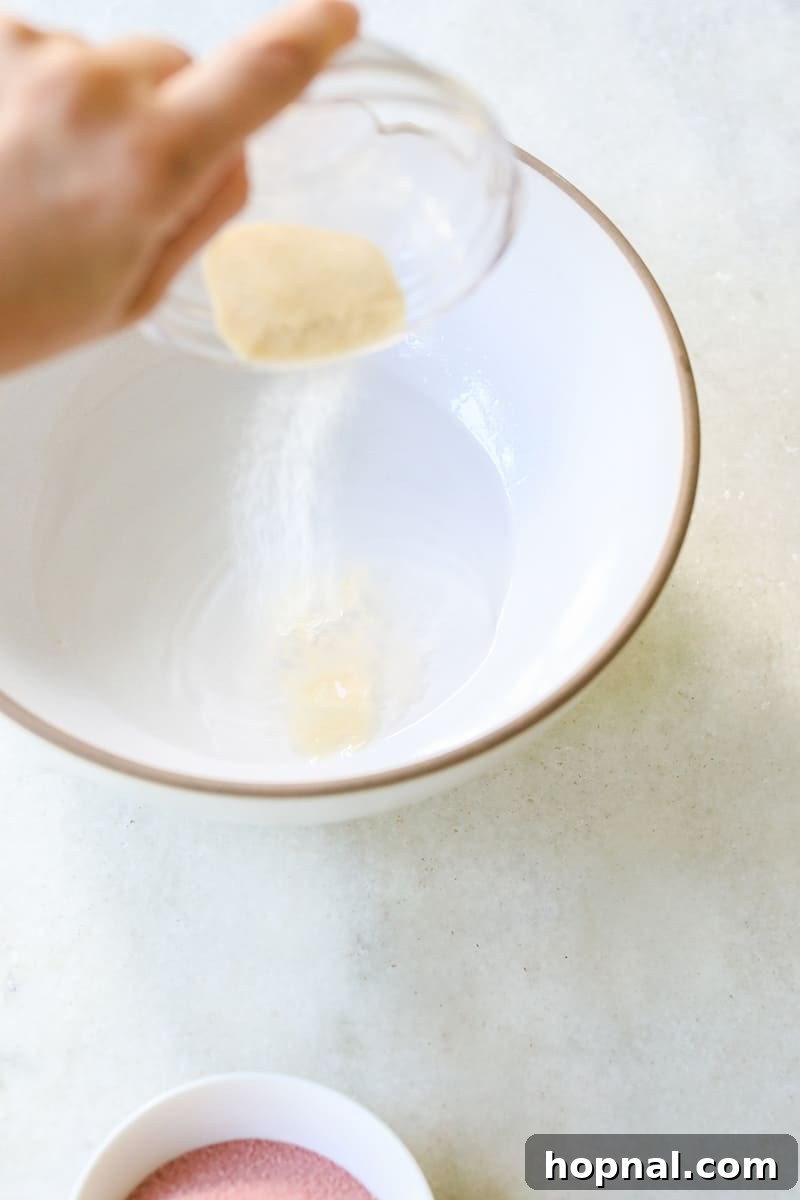The process of pouring unflavored gelatin powder into a white bowl containing vodka, a vital step in preparing jello shots.