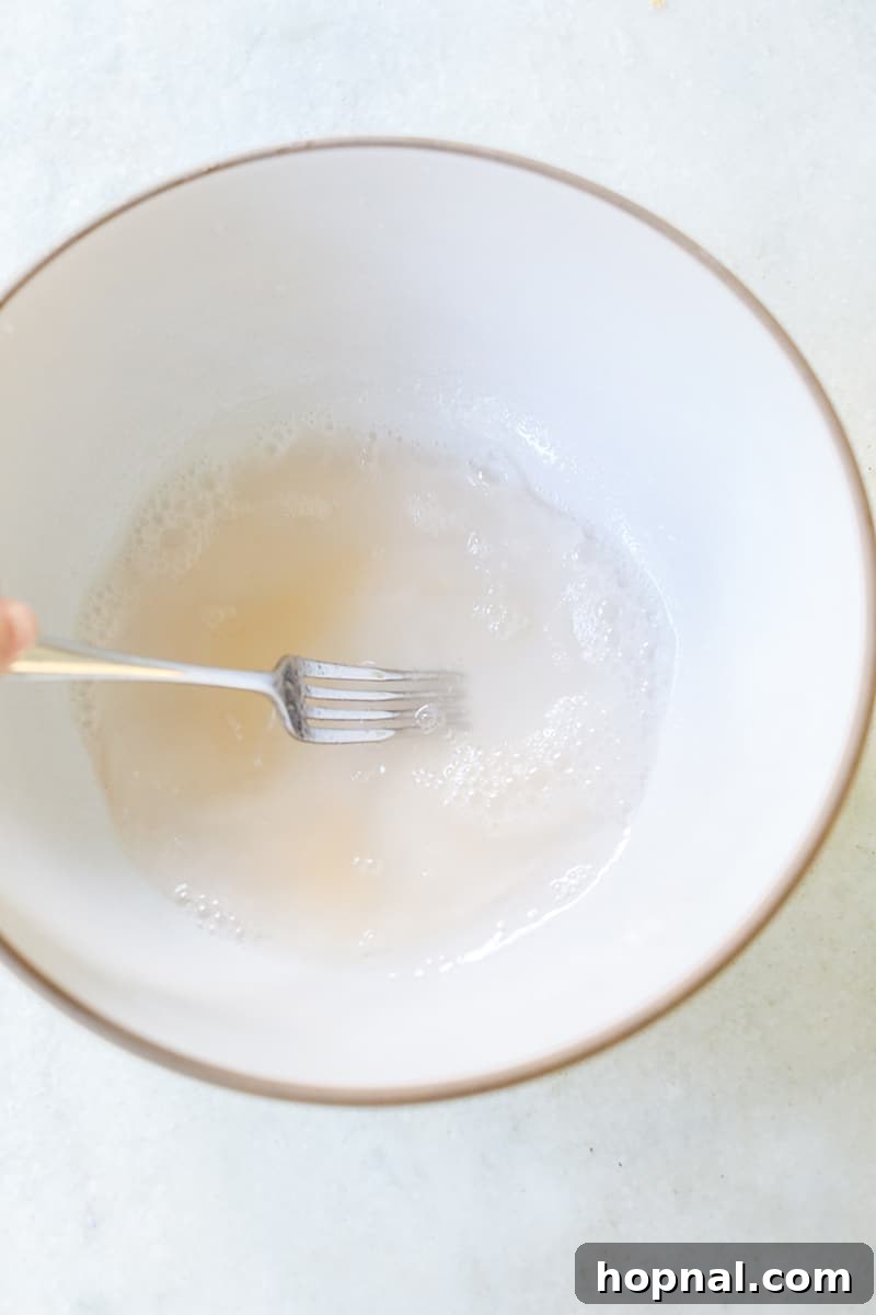 A fork is used to whisk unflavored gelatin into vodka in a white bowl, initiating the jello shot recipe.