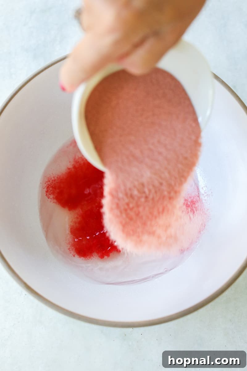 Adding red jello powder to a bowl that already contains a mixture of vodka and gelatin.