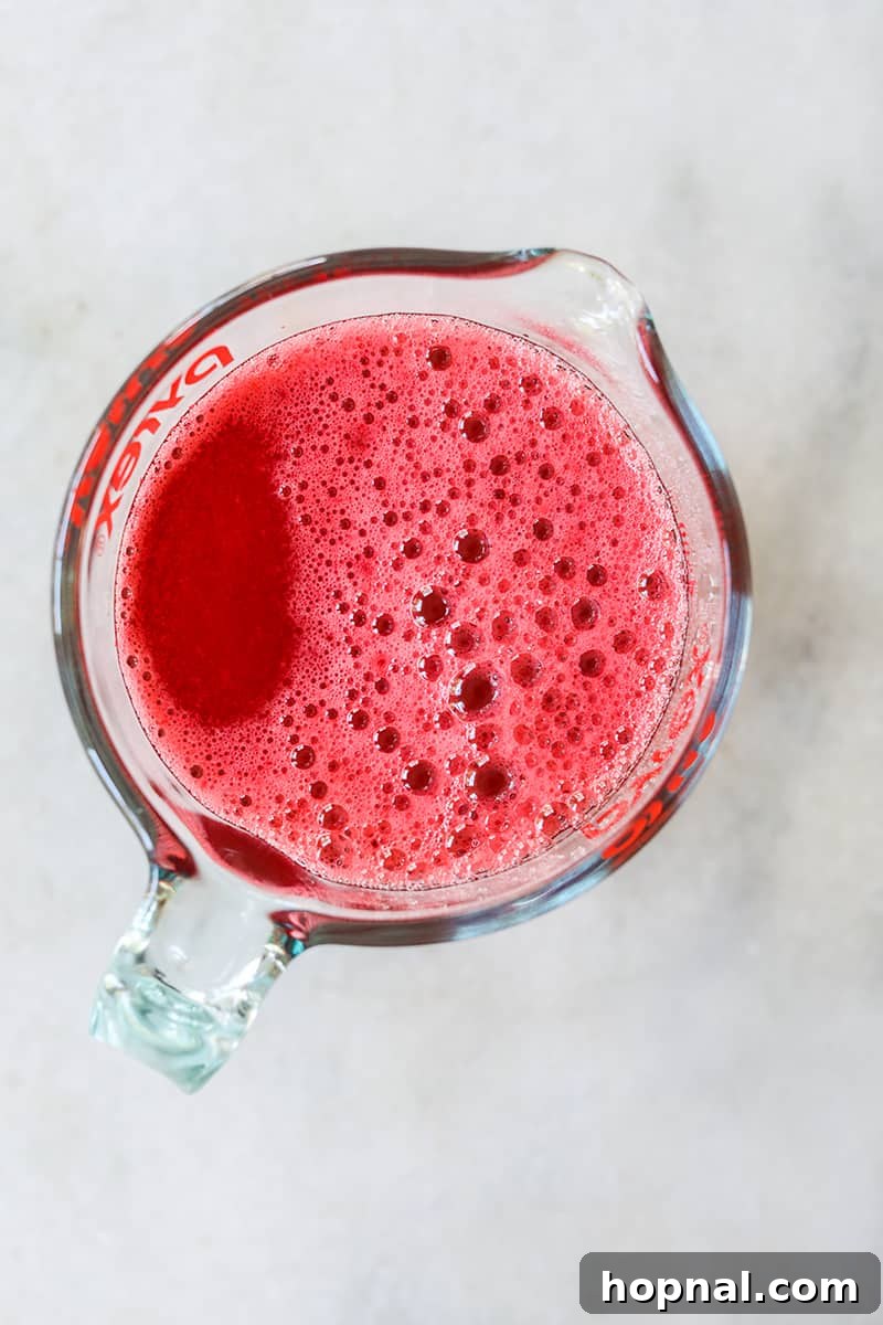 The liquid red jello mixture is held in a clear measuring glass with a spout, perfectly ready for careful pouring into molds.