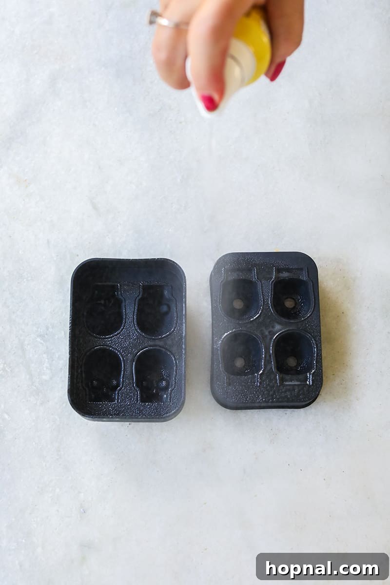 A skull gelatin mold is being sprayed with cooking spray, a crucial step before adding the liquid jello mixture to ensure easy release.
