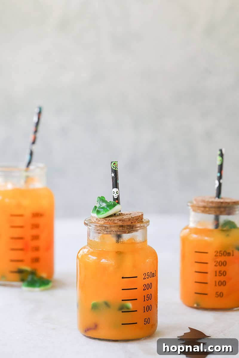 Vibrant green Halloween kids party punch served in glass jars with festive Halloween straws and fun frog gummies.