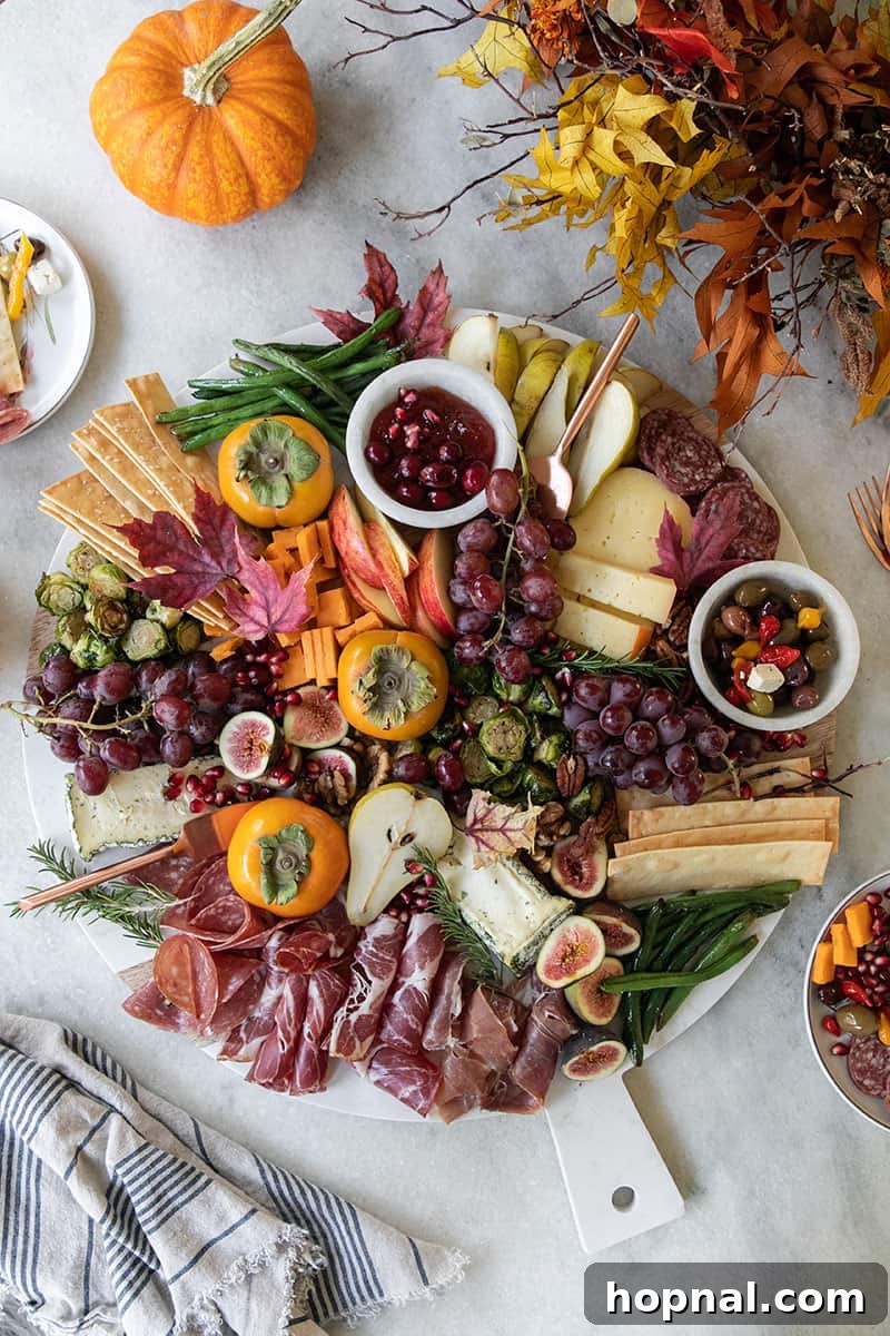 A Thanksgiving appetizer cheeseboard with fruit, cheese, meat, crackers, olives and more. On a marble table with fall leaves.