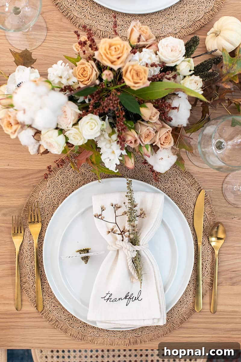 A beautifully arranged Thanksgiving table setting featuring white napkins, elegant white plates, lush floral arrangements, sophisticated gold flatware, and sparkling wine glasses.