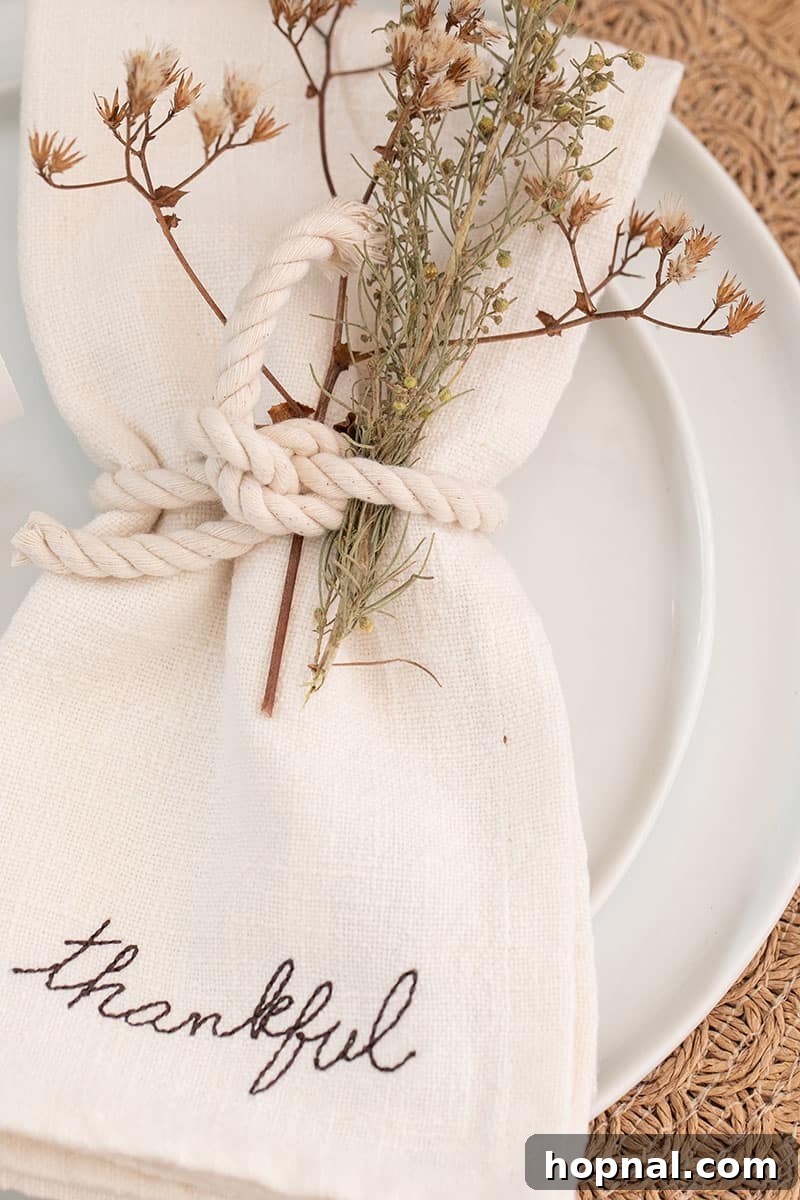 A close-up of a linen napkin adorned with the word 'thankful,' stylishly tied with a piece of rustic rope, perfect for a personalized Thanksgiving table setting.