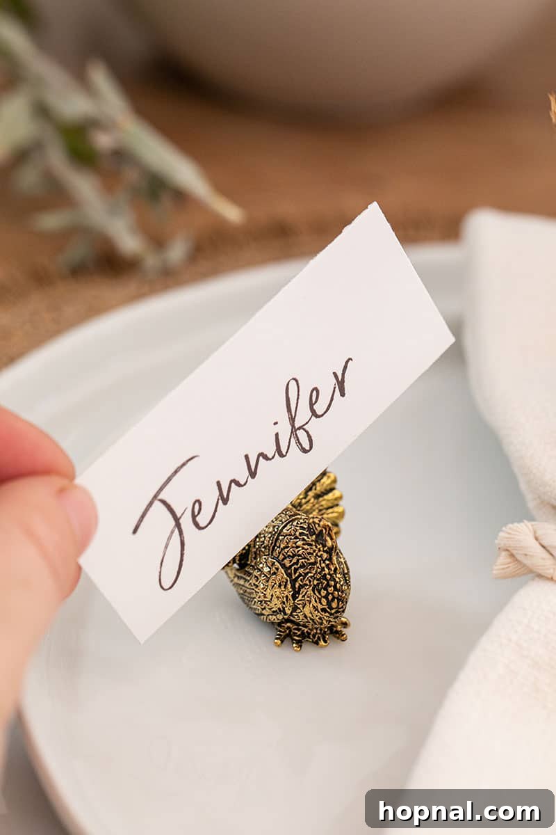 A hand placing a simple name card into a charming gold turkey holder, ready to personalize a Thanksgiving place setting.