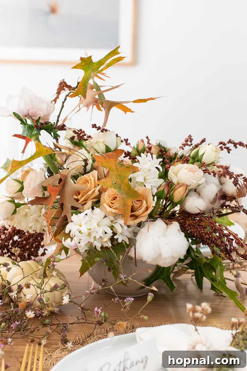 A lush fall flower arrangement, featuring seasonal blooms, leaves, and cotton, serving as a beautiful centerpiece for a Thanksgiving table.