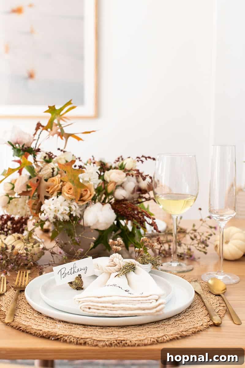 An elegant Thanksgiving table setting featuring a vase of fresh flowers, white wine glasses, crisp white plates, and neatly folded napkins, creating a refined atmosphere.