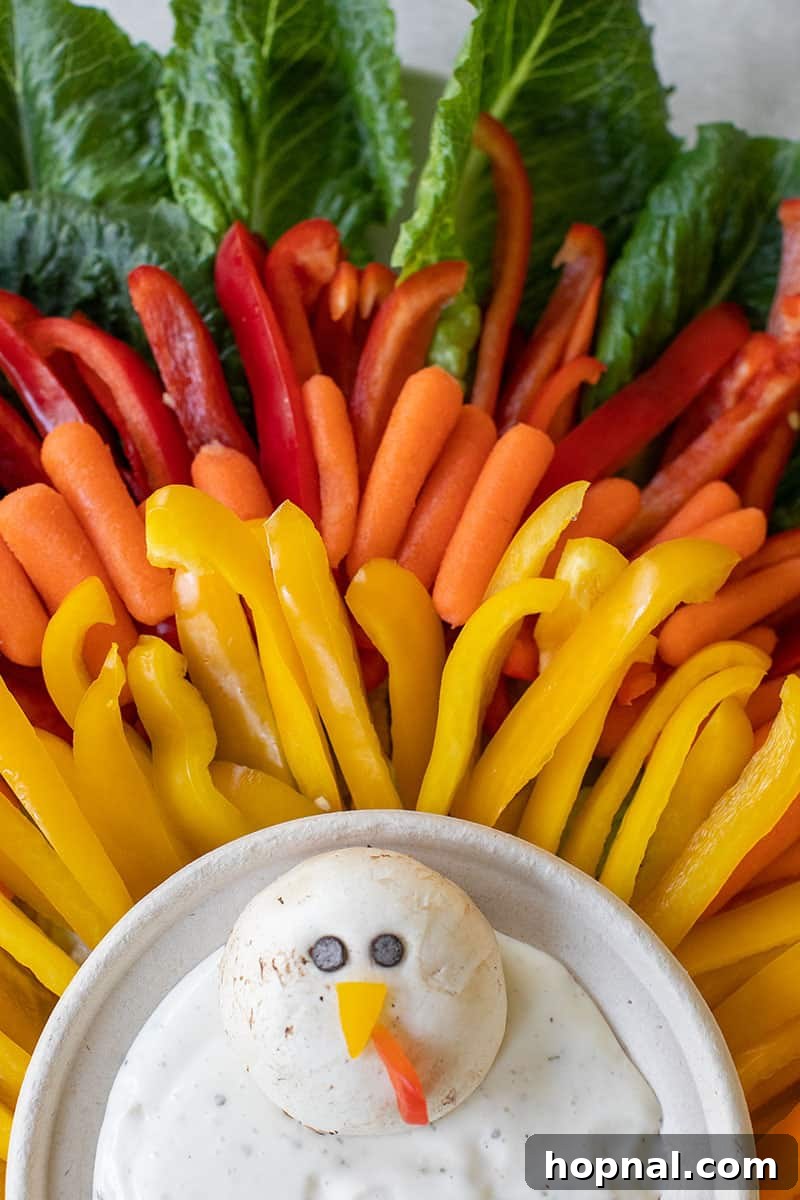 Colorful vegetables, including red bell peppers, baby carrots, and green lettuce, artistically arranged on a platter to form the beginnings of a festive Thanksgiving turkey.
