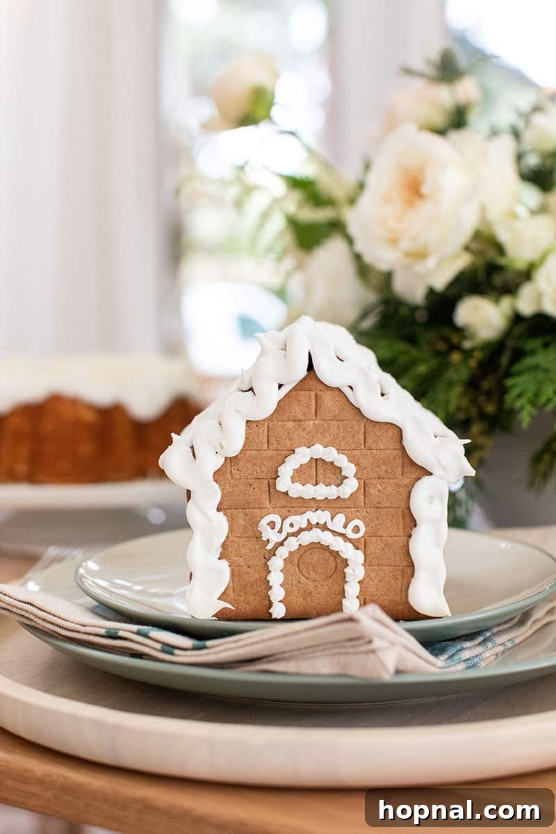 A gingerbread house, bearing the name 'Romeo' in frosting, beautifully integrated into a Christmas table setting.